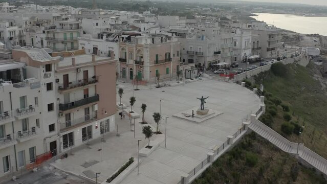 Aerial circle view with descending orbit on the coast with statue of Domenico Modugno. Polignano a Mare. Italy