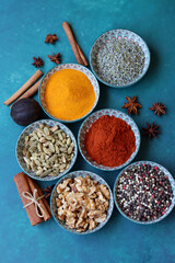 Close up photo of spices and herbs in blue ceramic bowls. Paprika, turmeric, anise, lavender, cardamom, cinnamon, pepper on textured blue background. 