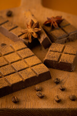 Chocolate with cinnamon, coffee beans and star anise on a brown background.