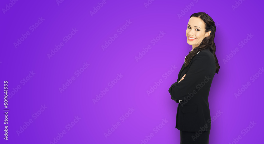 Wall mural Happy smiling attractive businesswoman, with copy space area for some slogan or advertising text. Confident brunette woman in black suit standing on violet purple background. Business ad concept.