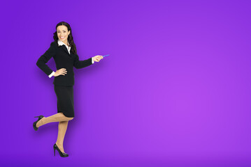 Full body length size view of happy excited smiling businesswoman showing pointing advertise at copy space. Confident business woman in black suit stand dancing on violet purple background.