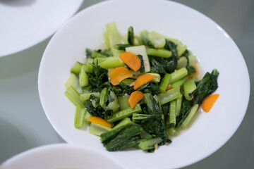 Home cook fried “choy sum” (chinese cabbage) on white bowl on glass table