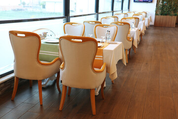 A restaurant consisting of brown wooden chairs and a table with a white fabric cover. Empty catering plates and forks, spoons, knives on a white tablecloth.	
