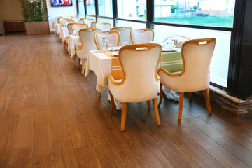 A restaurant consisting of brown wooden chairs and a table with a white fabric cover. Empty catering plates and forks, spoons, knives on a white tablecloth.	
