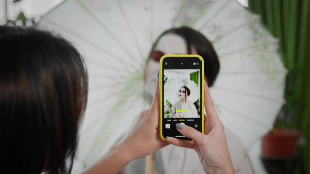 Women's hands are photographing a girl in the form of a geisha on the phone. Creating an image for a photo shoot