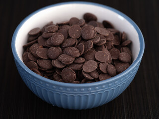 A pile of chocolate chips in a bowl. Low key. Close up.
