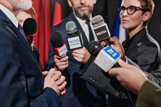 Close-up of group of journalists holding microphones in front of businessman and interviewing him at conference