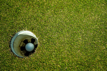 Golf ball in hole on a green lawn in a beautiful golf course with morning sunshine.