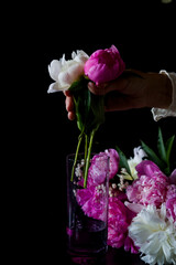 wine and flowers. still life with flowers. Bouquet of white and pink peony on a black background. Flower in a glass of water. Hand holding a glass
