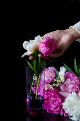 wine and flowers. still life with flowers. Bouquet of white and pink peony on a black background. Flower in a glass of water. Hand holding a glass