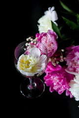wine and flowers. still life with flowers. Bouquet of white and pink peony on a black background. Flower in a glass of water