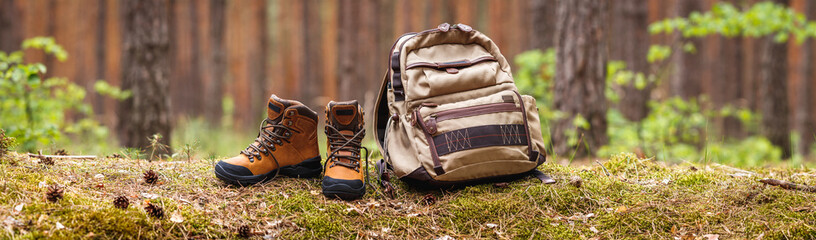 Hiking equipment in forest. Backpack and leather ankle boots. Panoramic view with copy space 