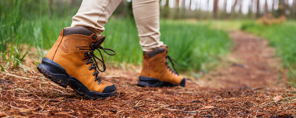 Tourist with hiking boots walking on footpath in forest. Trekking trail in woodland. Waterproof...