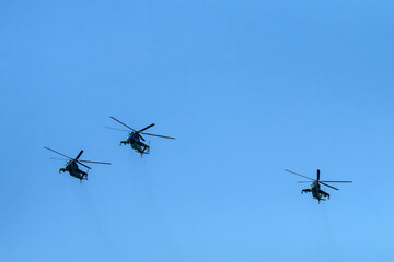 Fototapeta na wymiar The flight of three soviet battle helicopters, type MIL Mi-24 flying on the bright blue sky.