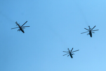 The flight of three soviet battle helicopters, type MIL Mi-24 flying on the bright blue sky.