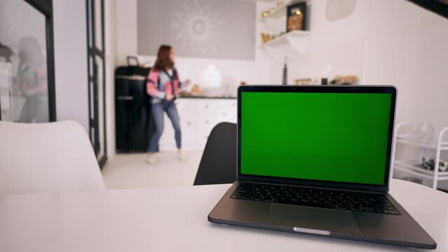 in the foreground laptop with green screen in the background defocused woman dancing in the kitchen happy time at home