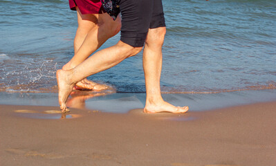 Sea in sunny weather. Legs of people who walk along the sea