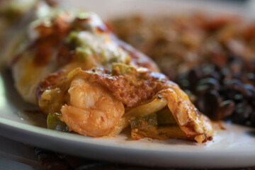 Side and closeup View of shrimp enchiladas on white plate.