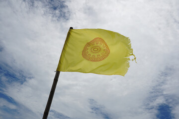 Yellow Buddhist flag (Dhammachakka flag) is torn at the edge of the flag flying on the sky background.
