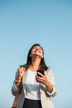 Business woman celebrates winning with her smart phone in her hand. Vertical image of a woman celebrating success. Copy space