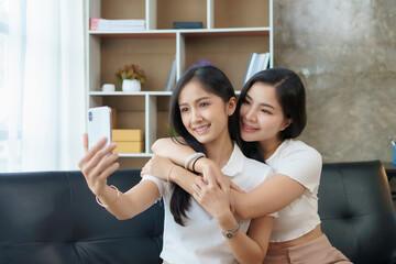 Asian lesbian couple, LGBTQ. Lesbian couple holding smartphone and posing while making selfie together. Happy two young Asia women showing love and romance together at home.