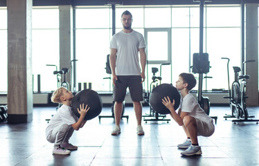 Children's fitness. Two teenager boys are training with a trainer in a modern gym. Training with mid balls, functional training. Healthy lifestyle
