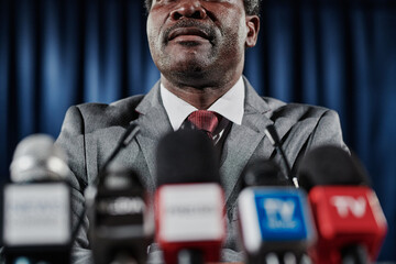 Close-up of African mature speaker standing opposite mcrophones at press conference for television