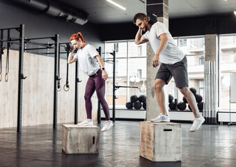Obraz premium Athletic man and woman practicing lunges together with dumbbell on box in modern gym