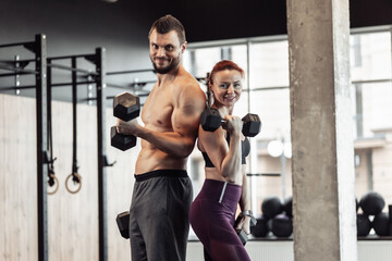 Fototapeta na wymiar Athletic couple man and woman with dumbbells in their hands posing in gym