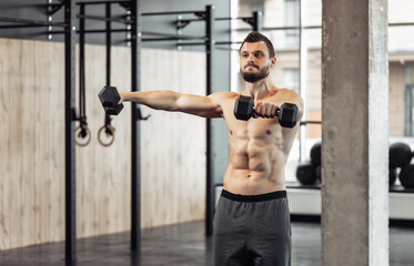 Fototapeta na wymiar Athletic man with a naked torso trains his shoulders with dumbbells in his hands. Workout in the gym. Bodybuilding and fitness, healthy lifestyle