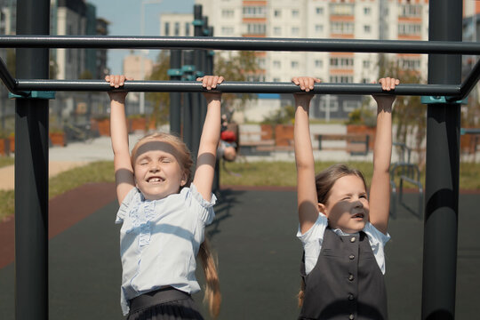 Two little schoolgirls jumping onto the monkey bars at a playground in schoolyard. Schoolmates wearing school uniform and play during school break.