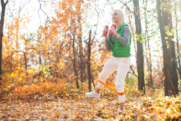 Active and energetic fit blond woman is training with dumbbells and fitness band in the autumn forest. Healthy lifestyle. Outdoor workout