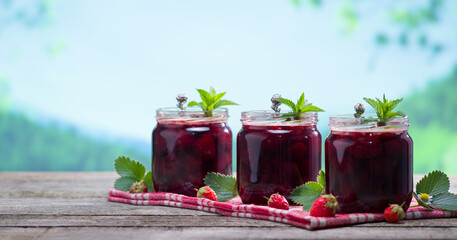Strawberry jam jars on wooden table. Homemade delicious organic strawberry jam with nature background. Healthy breakfast concept.
