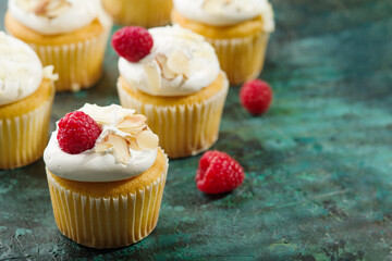 Many delicious muffins with cream, raspberries and almonds on a green background. There are no people in the photo. There is free space to insert. Holiday, birthday, banquet.
