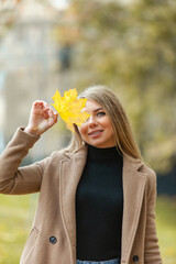 Cute cheerful blonde woman with fallen yellow leaf closing her eyes. Autumn time