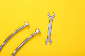 Metal hose with wrench on a yellow background. The work of plumber. Top view. flat lay