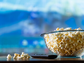 Close-up. Popcorn in a bowl on a blue background and a TV remote control. There are no people in...