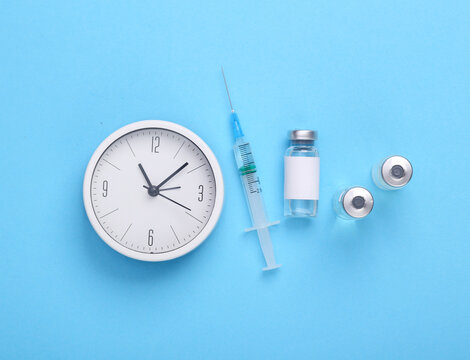 Vaccine bottle with a blank label for the brand and syringe with cock on blue background. Covid 19 vaccination