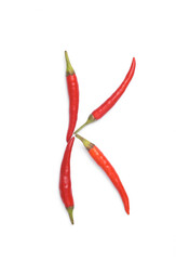 Letter K made from red chilli peppers isolated on white background