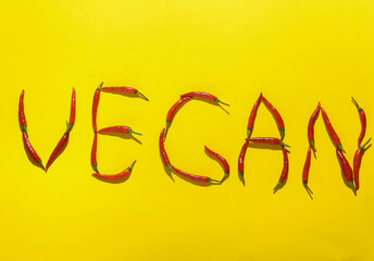 Word vegan made from red chili peppers on yellow background