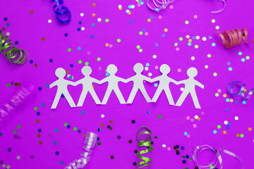 Chain of paper cut people with colored streamers and confetti on pink background. Celebrating Unity