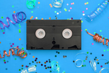 Video cassette and colored streamer with confetti on blue background. Movie day