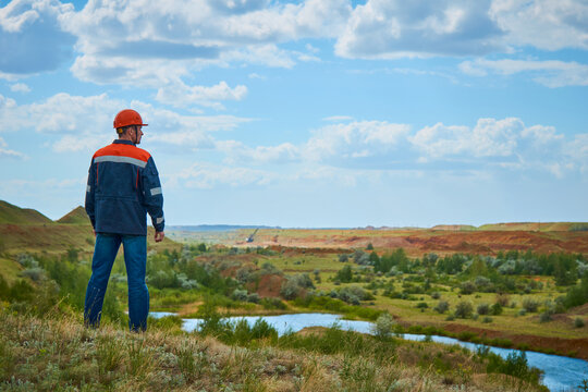 A mining engineer in a helmet and protective suit stands against the background of the mine and looks away