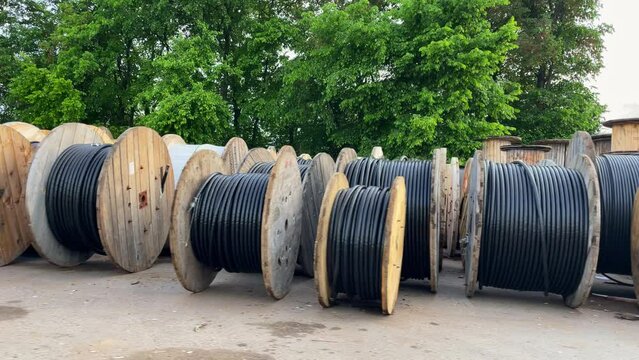 Lots of big wooden coils with black cable. Coils with cable in a street warehouse. High and low voltage cables.