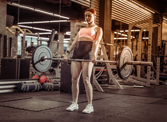 Fototapeta na wymiar Strong fit woman doing deadlift exercise with a barbell in a modern gym. Intense workout