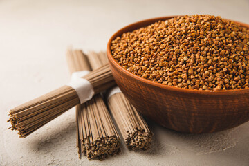 Buckwheat porridge in a bowl and buckwheat soba noodles on a white marble background. Raw...
