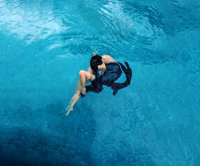 Top view of a beautiful young sexy blonde women relaxed in black dress floating flying weightless elegant in erotic dream turquoise water of the spa pool