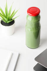 fresh green smoothie on desktop with laptop and flower on white background. Healthy snack in office. copy space. healthy lifestyle concept. 