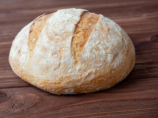 Close-up of a round loaf of wheat bread lying on a brown wooden background. Baking, bakery concept. Side view