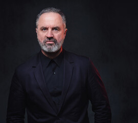 Portrait of handsome elderly dressed in black formal clothes with stylish hairstyle against dark background.